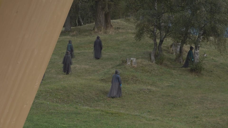 Menschen in dunklen Gewändern gehen auf einer Wiese.