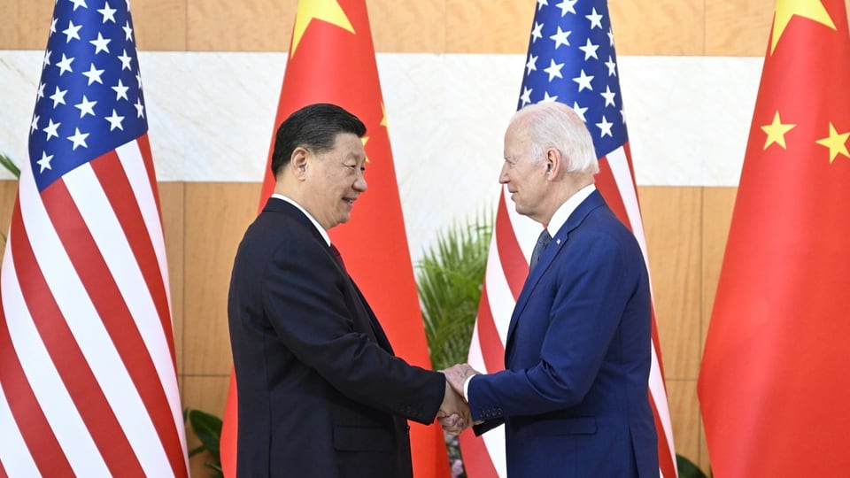 Die beiden Präsidenten aus China und den USA schütteln sich die Hand vor Flaggen der USA und China.