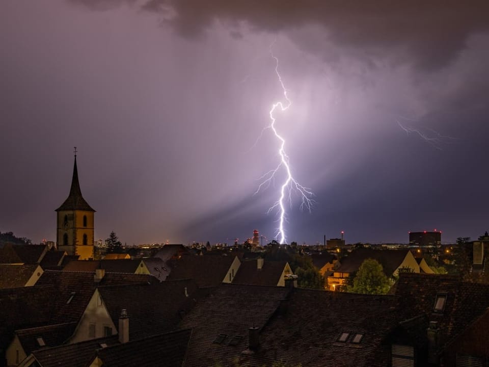 Blitz über einer nächtlichen Stadtsilhouette mit Kirche.