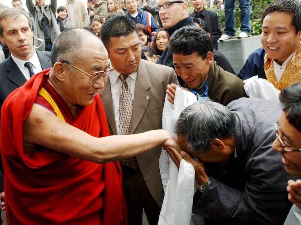 Eine Person küsst die Hand von Dalai Lama