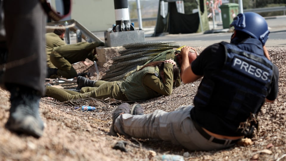 Pressevertreter fotografieren israelische Soldaten, die sich am Boden decken.