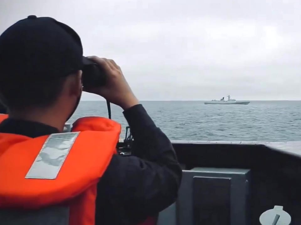 Eine Person auf einem Schiff beobachtet ein anderes Schiff auf weiter See durch ein Fernglas.