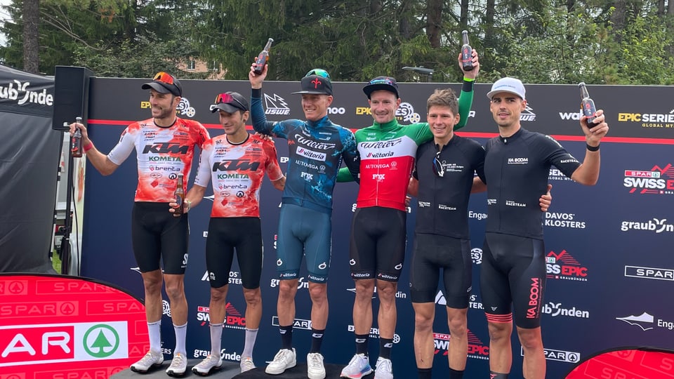 Sechs Radfahrer auf einer Siegerehrungsbühne mit Trophäen.