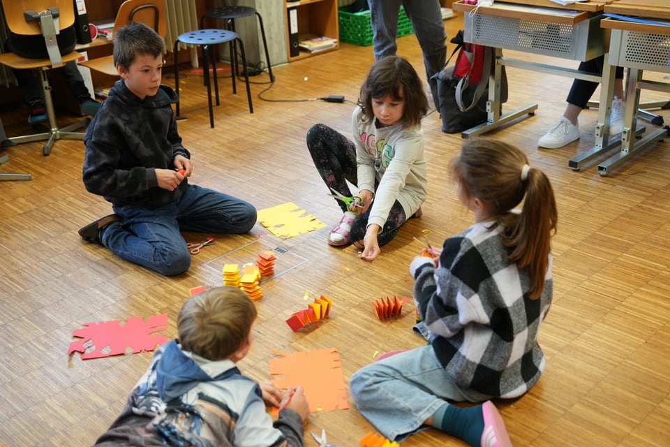 Kinder basteln im Klassenraum am Boden.