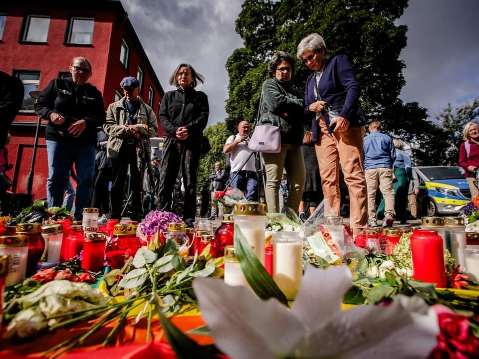 Menschen trauern vor Kerzen und Blumen bei einer Mahnwache im Freien.