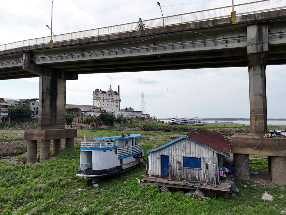 Brücke über Fluss mit altem Boot und Haus am Ufer.