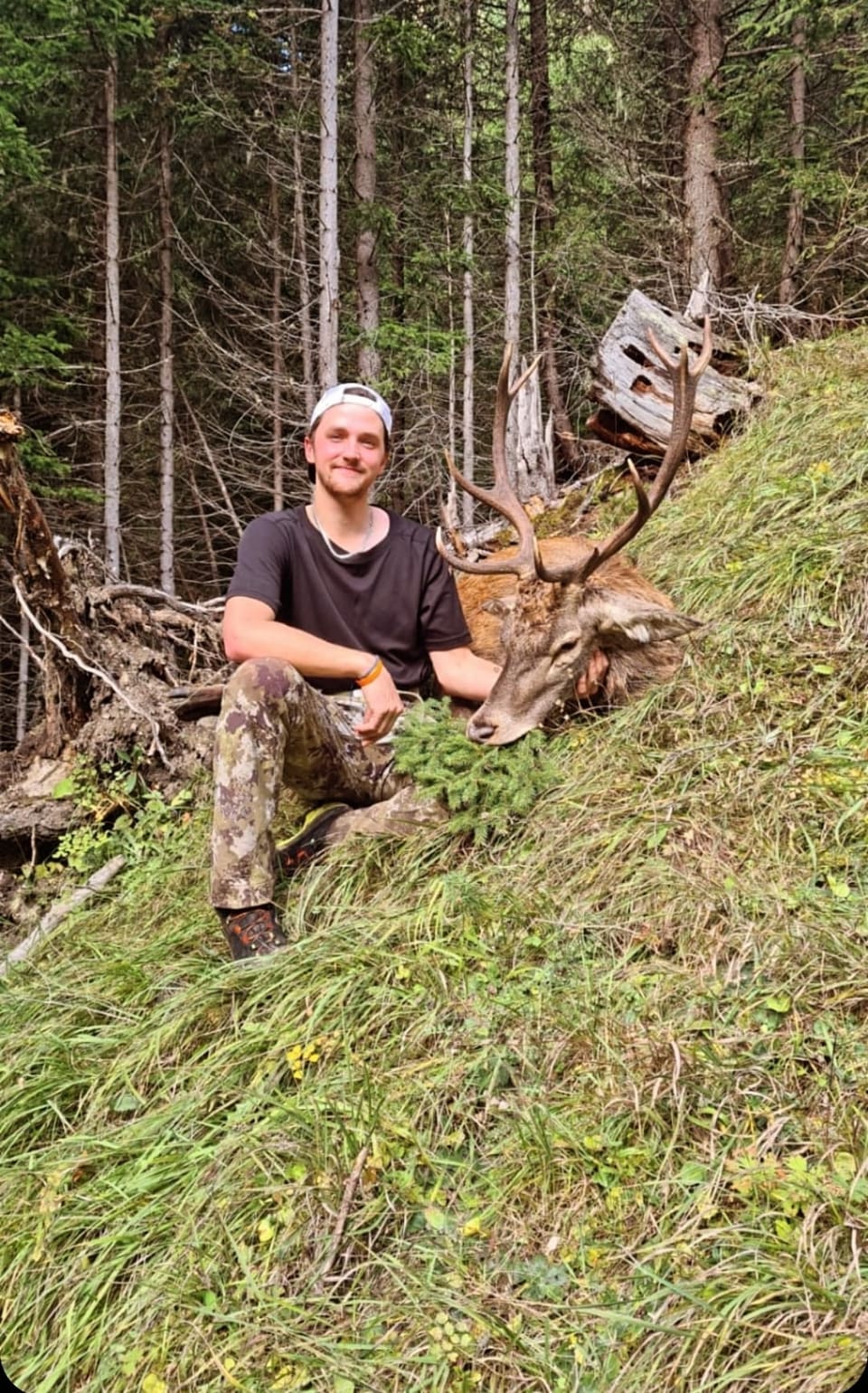 Jäger posiert im Wald neben erlegtem Hirsch.