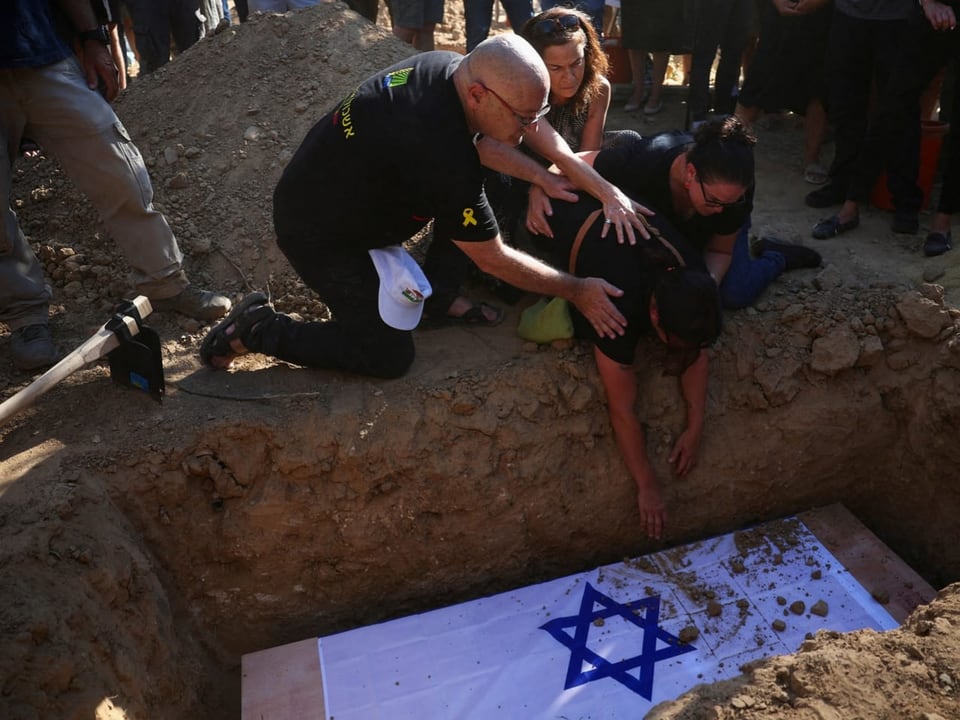 Menschen bei einer Beerdigung legen eine Hand auf einen mit einer israelischen Flagge bedeckten Sarg.