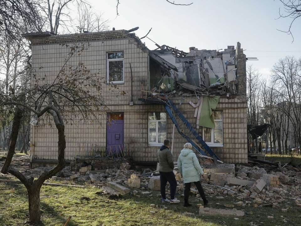Zwei Personen stehen vor einem stark beschädigten Gebäude.