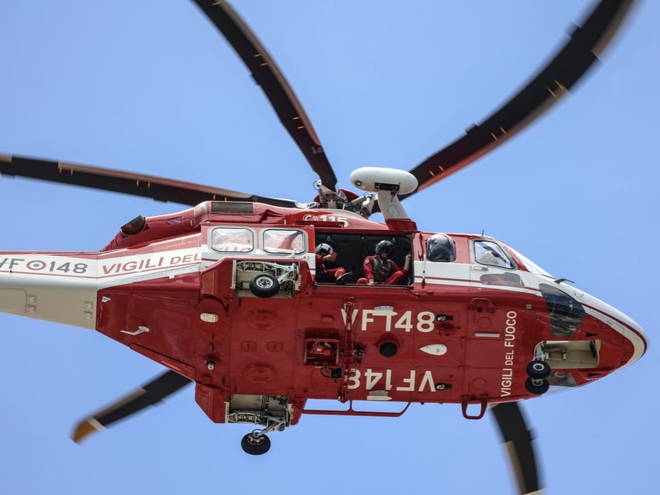 Roter Hubschrauber der Feuerwehr im Flug vor blauem Himmel.