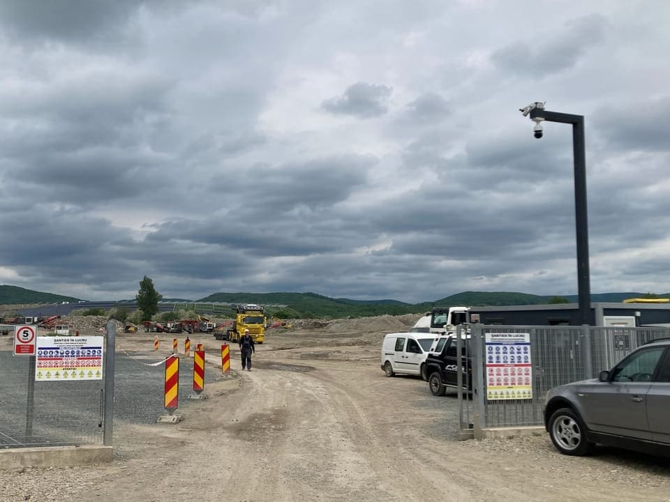 Baustelle unter bewölktem Himmel mit Fahrzeugen und Bauzäunen.