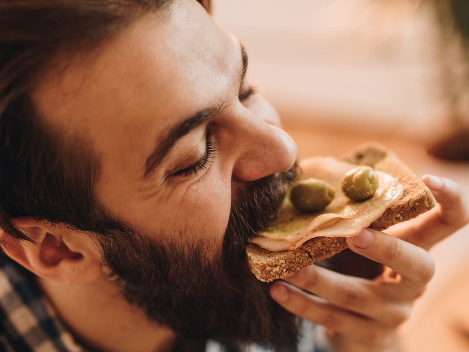 Ein Mann beisst genüsslich in ein Toast mit Schinken und Oliven