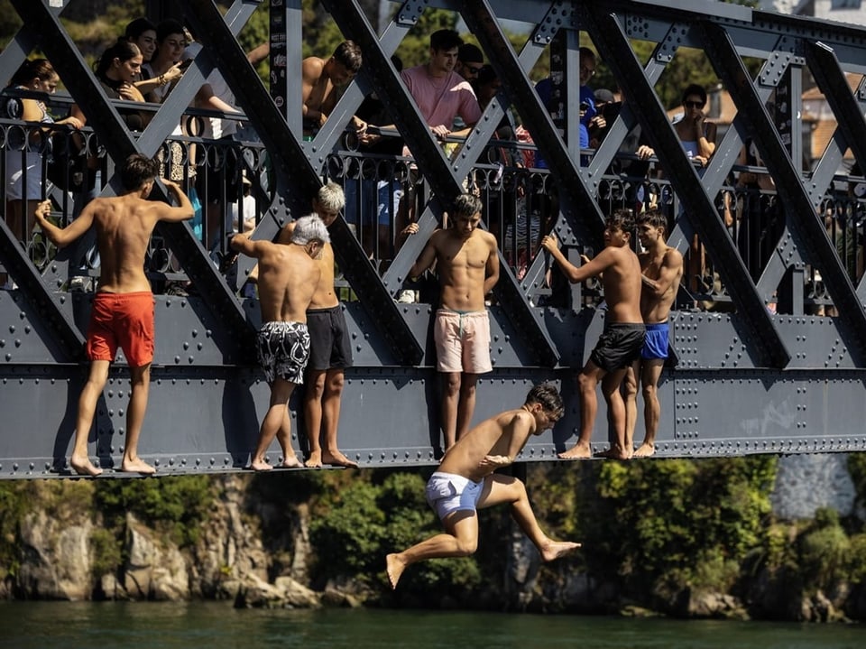 Gruppe junger Männer springt von einer Brücke ins Wasser.