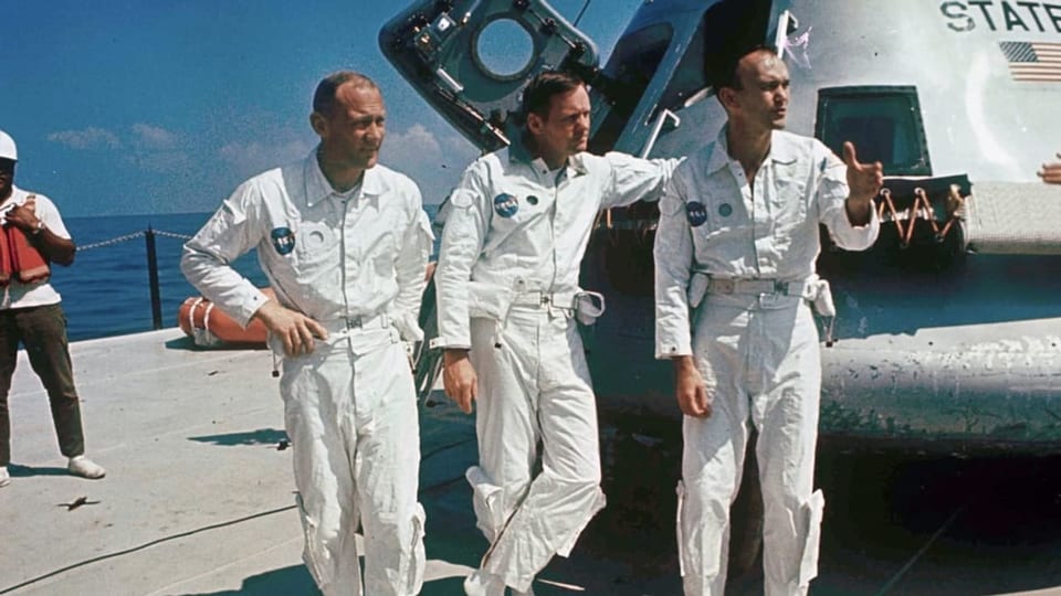 Drei Männer in weissen Anzügen der Nasa neben ihrem Raumfahrzeug