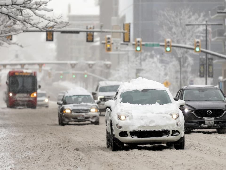 Autos auf der Strasse haben Schnee auf den Dächern. Die Strasse selbst ist ebenfalls schneebedeckt.