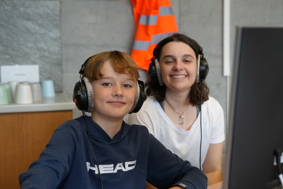 Junge und Frau mit Kopfhörern an einem Tisch.