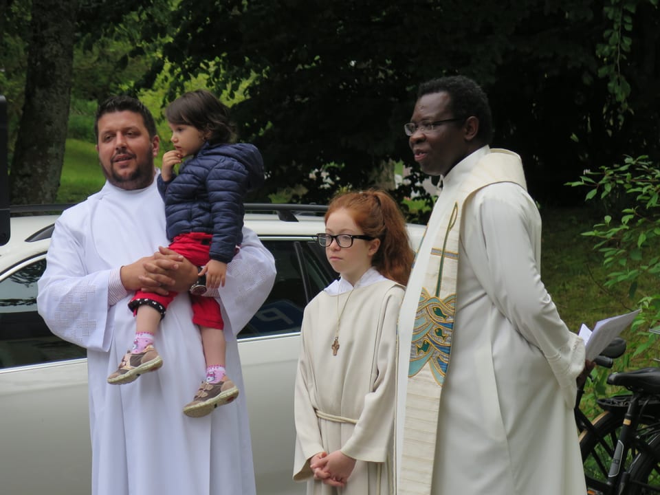 Pfarrer mit Ministrantin und Pastoral-Assistent der ein kleines Kind auf dem Arm hält. 