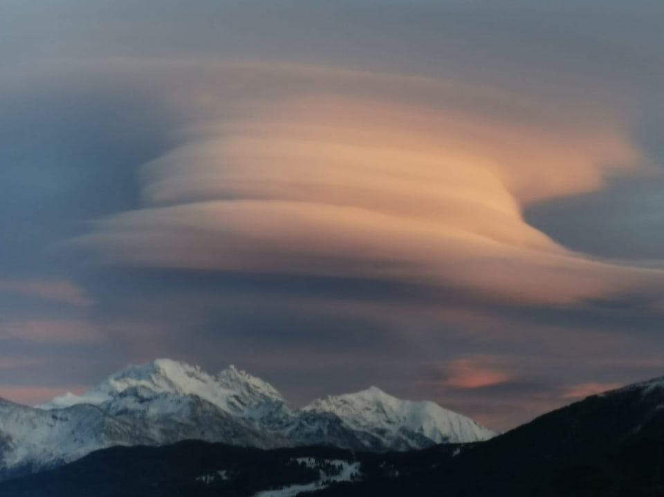 Lenticularis Wolken über schneebedeckten Bergen bei Sonnenuntergang.