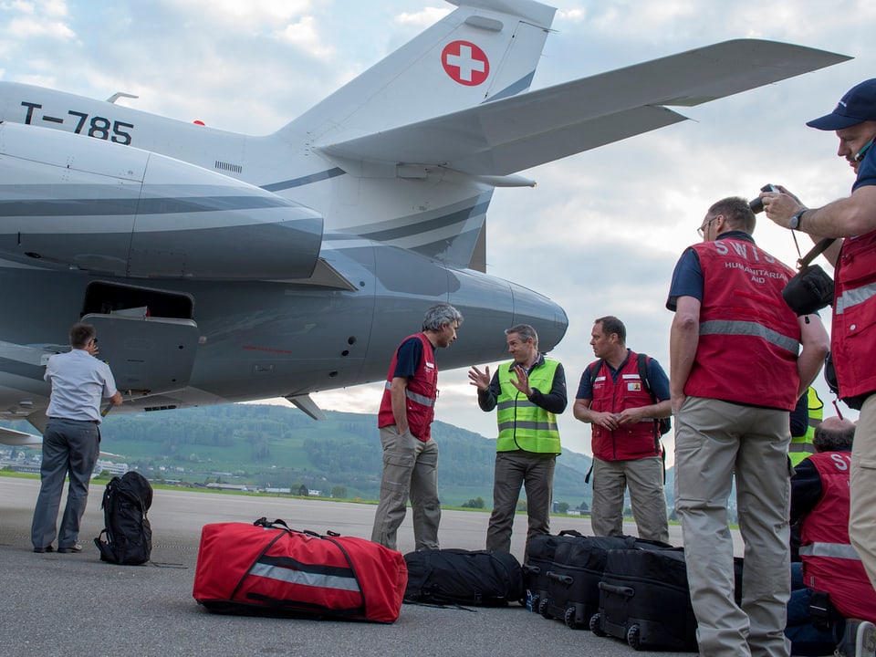 Männer in roten Westen stehen mit ihrem Gepäck vor dem Bundesrats-Jet und diskutieren.