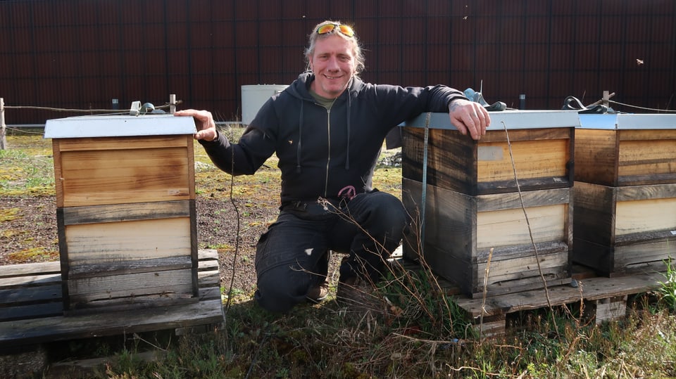 Lukas Riechsteiner kniet vor einigen Bienenstöcken.