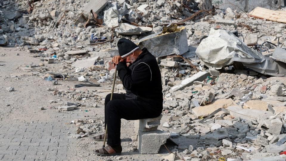 Ein Mann sitzt vor Schutthaufen zerstörter Gebäude im Gazastreifen.