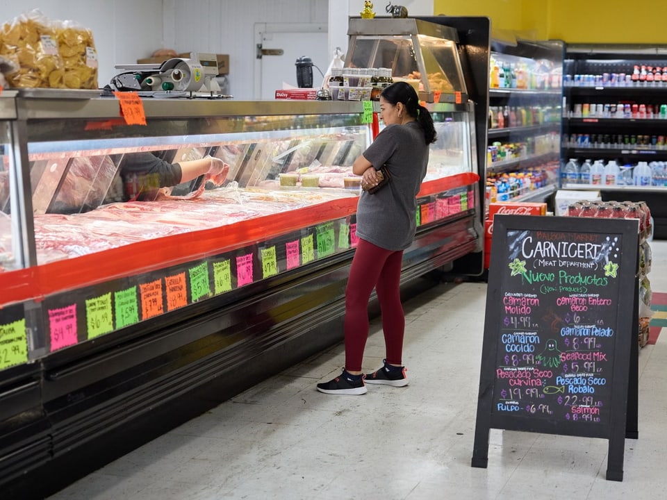 Frau steht vor Fleischtheke in Supermarkt.