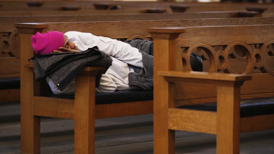 Ein Mann schläft auf einer Kirchenbank.