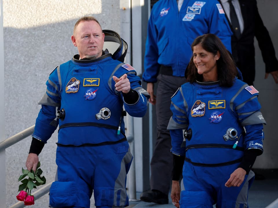 Zwei Astronauten in blauen Raumanzügen, einer hält Rosen.