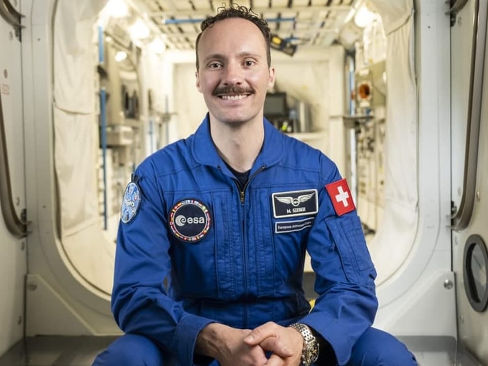 Astronaut in blauer Uniform sitzt in einem Raumschiffmodul.