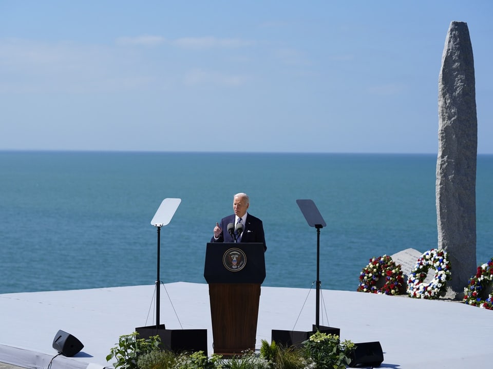 Person hält eine Rede vor einem Denkmal am Meer.