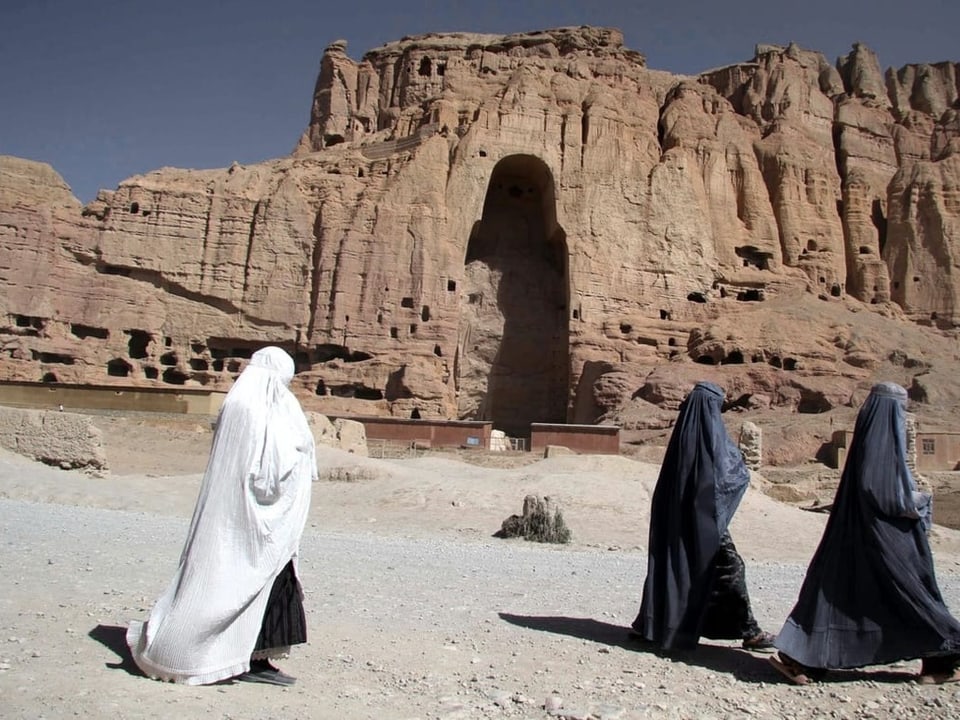 Drei Frauen laufen im Burka vor einer Ruine in Afghanistan vorbei