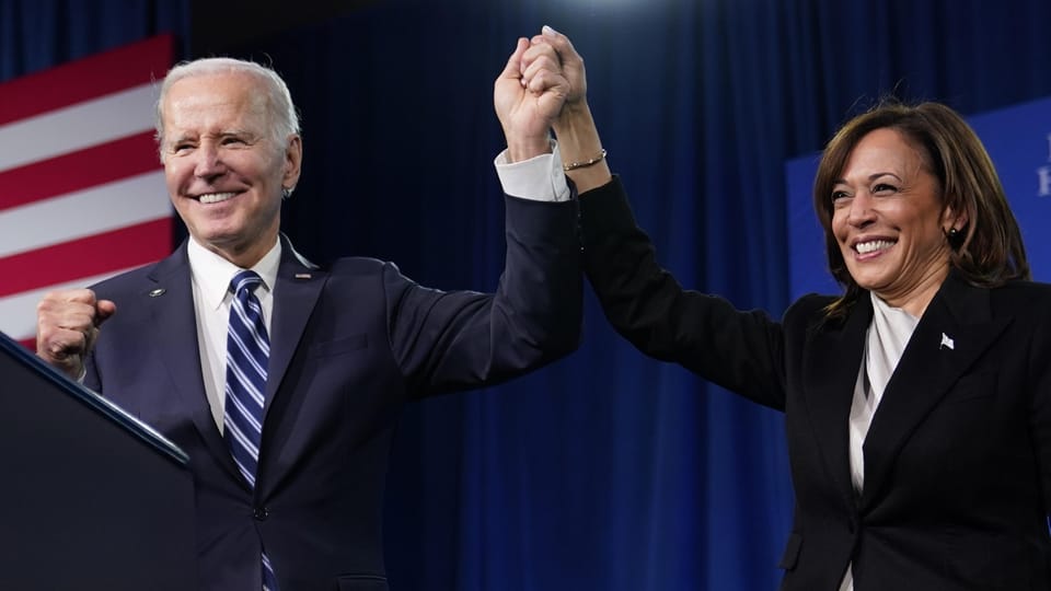 Joe Biden und Kamala Harris halten triumphierend Hände hoch auf Bühne.