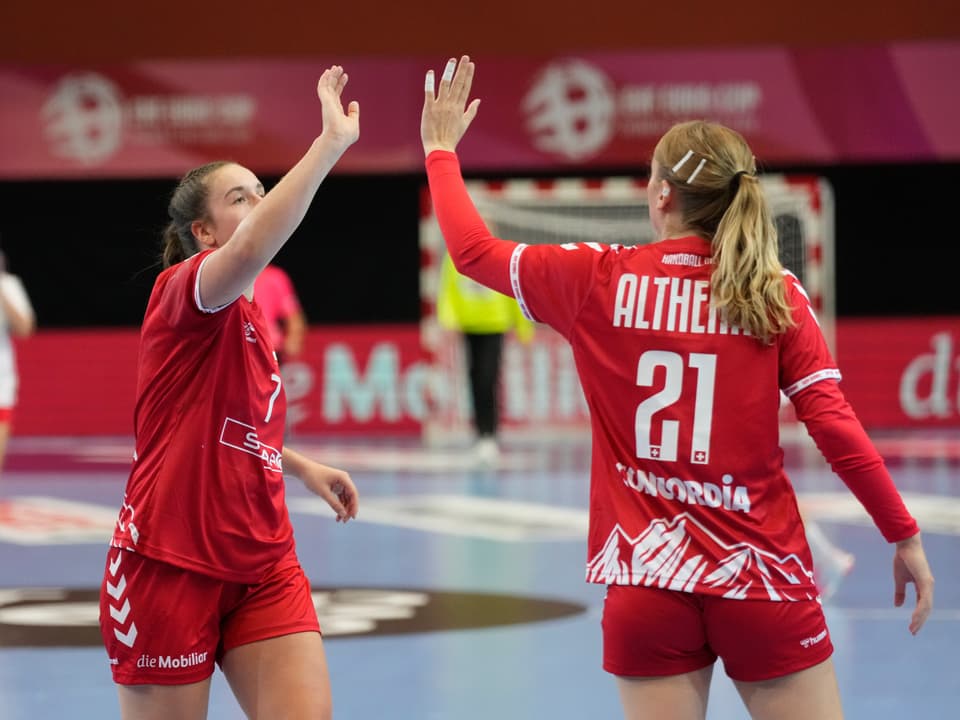 Zwei Handballspielerinnen klatschen auf dem Spielfeld ab.