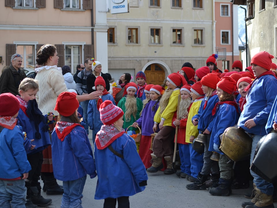 Kinder mit roten Mètzen, grossen Kuhglocken und blauen Jacken.. zum Teil mit Bärten aus Schafwolle.