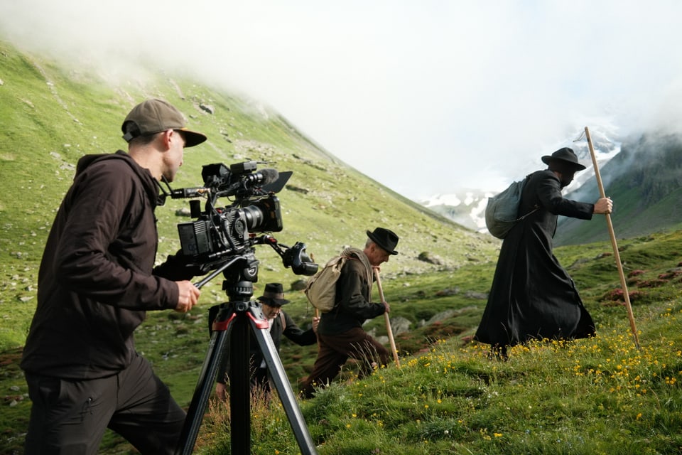 Kameramann filmt Wanderer in traditioneller Kleidung in bergiger Landschaft.