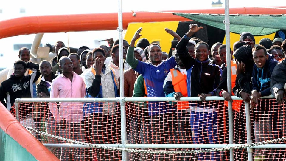 Junge schwarze Männer stehen auf einem Schiff, das in Italien ankommt.