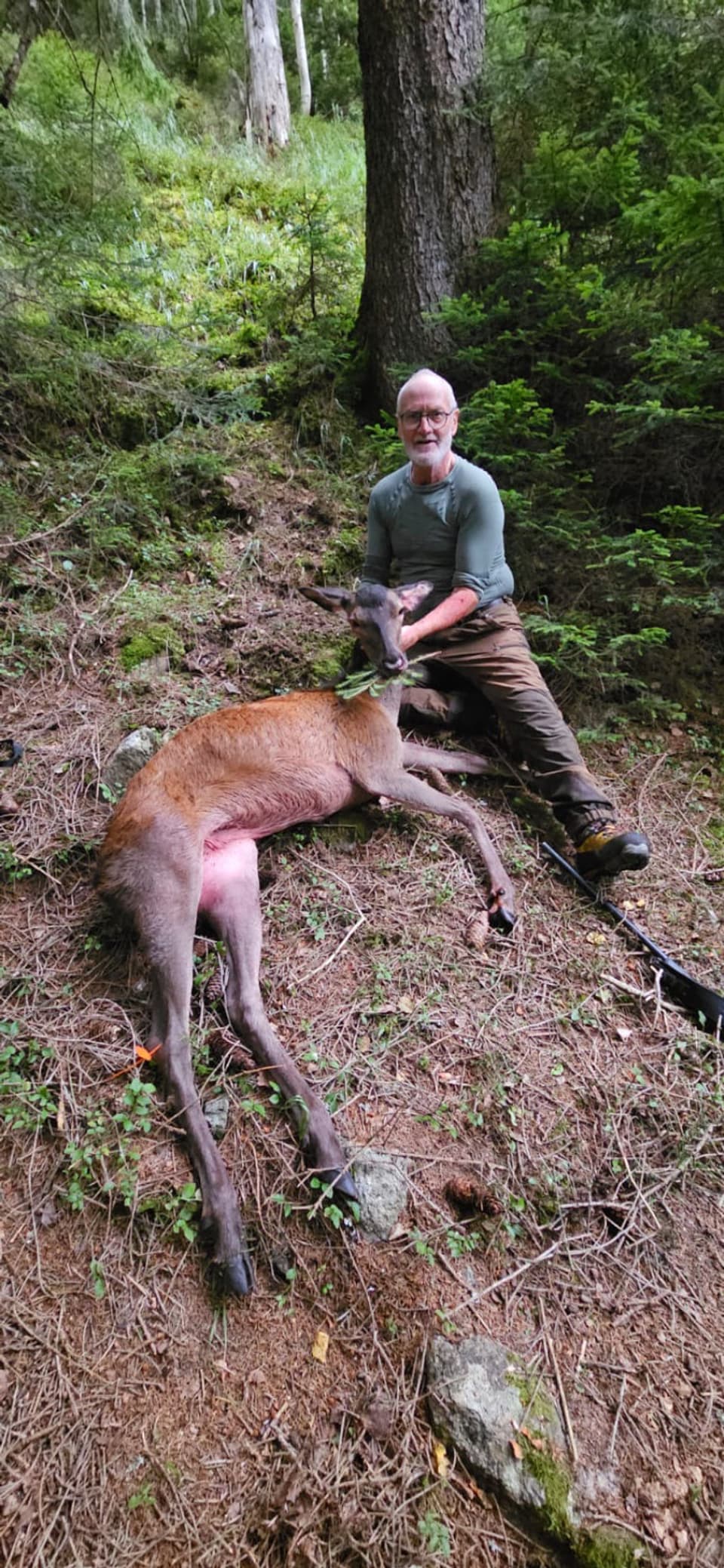 Mann sitzt neben erlegtem Hirsch im Wald.