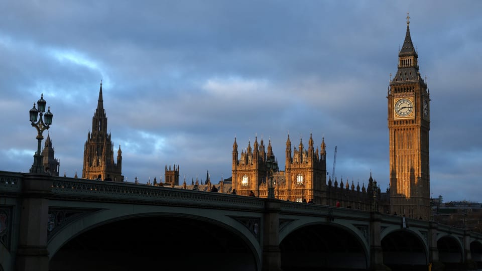 Brücke, dahinter Skyline mit rechts dem Big Ben Turm, links Kirche, alles in warmem Licht.