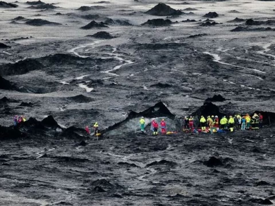 Menschen in Schutzkleidung auf einem vulkanischen Lavafeld.