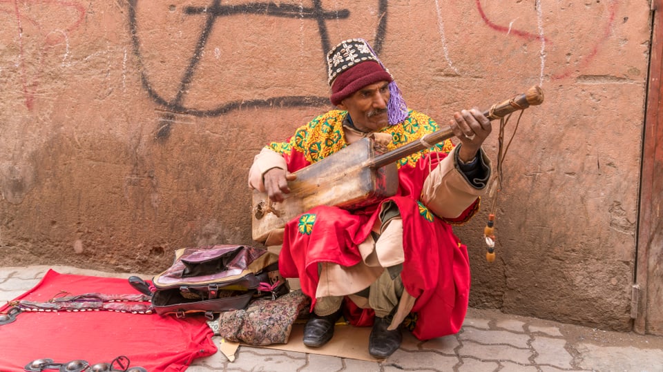 Ein Ein Strassenmusiker in langen, bunten Gewändern spielt in Marrakesch auf einer Laute.