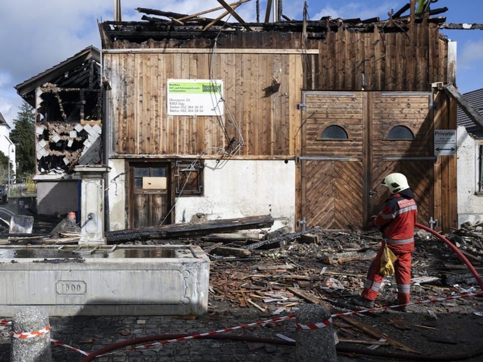 Feuerwehrmann steht vor abgebranntem Gebäude.