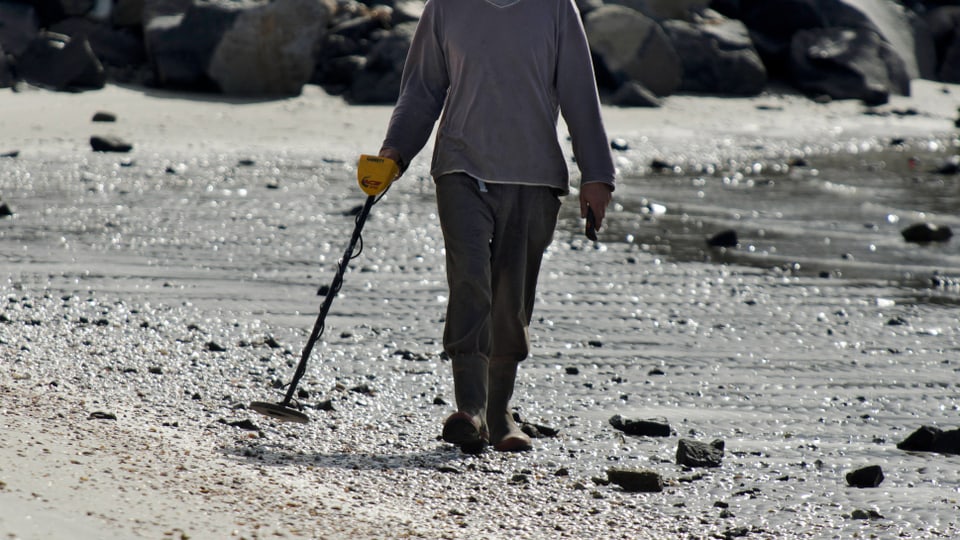 Person mit Metalldetektor am Strand.