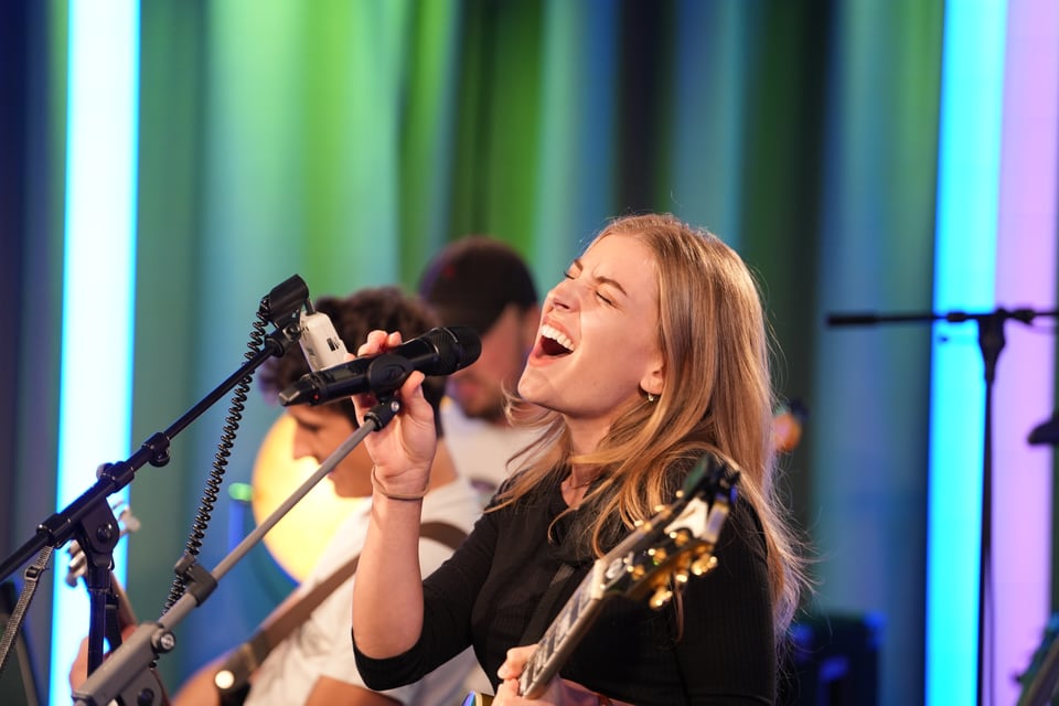 Frau singt und spielt Gitarre auf der Bühne.