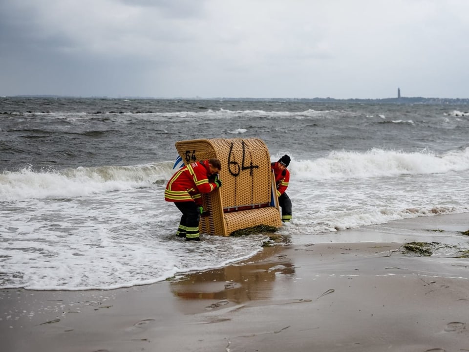 Zwei Männer verhindern, das ein Strandkorb von den Wellen mitgerissen wird.
