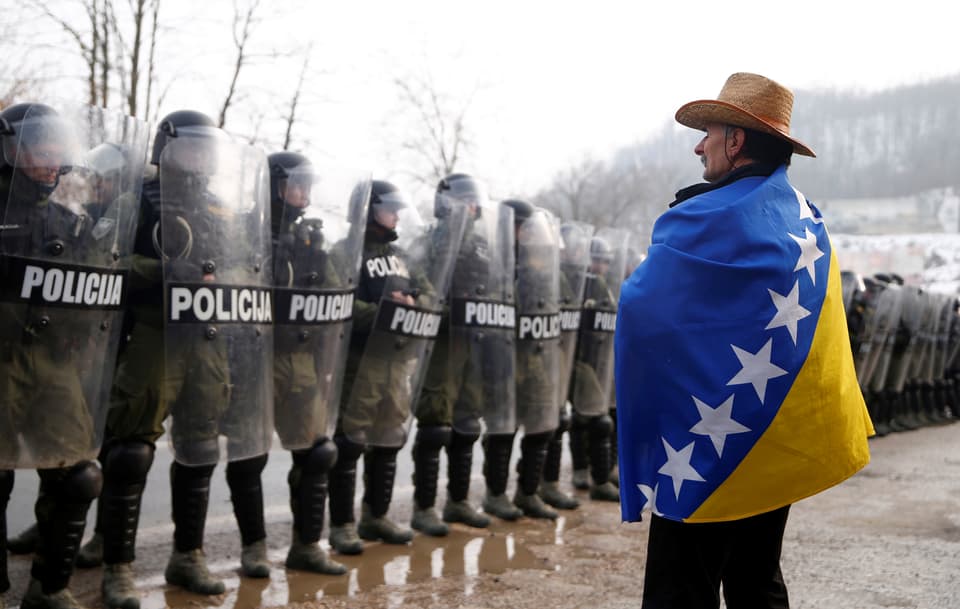 Eingehüllt in die Flagge Bosnien-Herzegovinas steht ein demonstrierender Veteran der Übermacht der Polizei gegenüber.