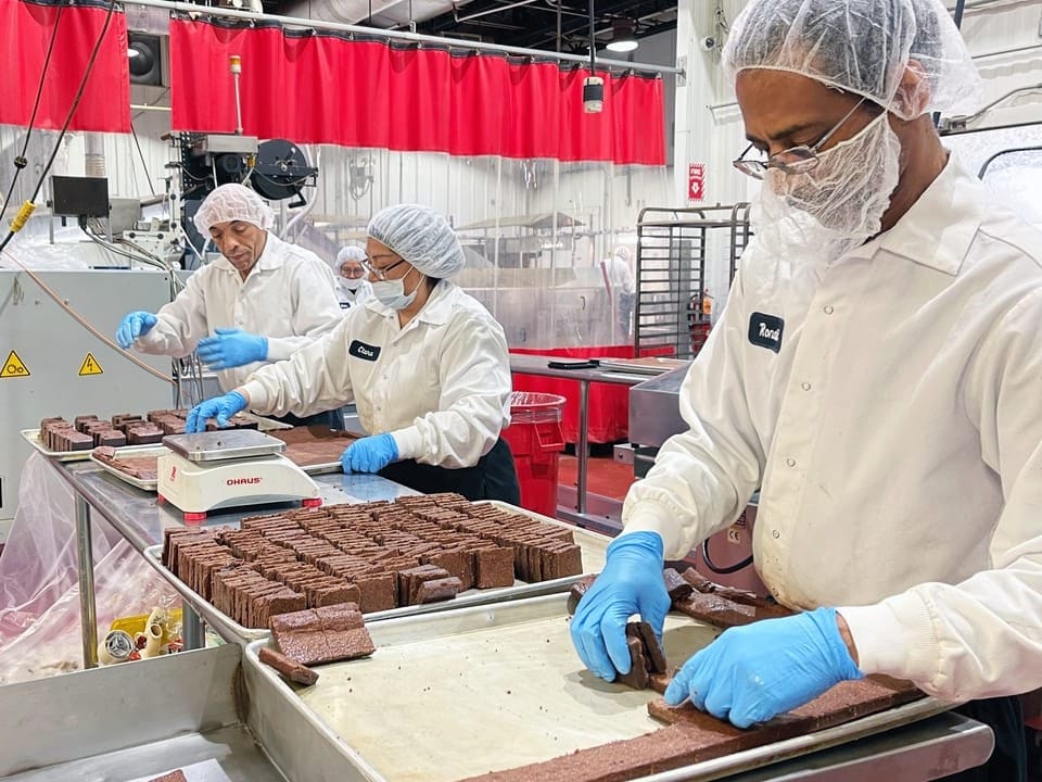 Drei Arbeiter in Schutzkleidung verarbeiten Lebensmittel in einer Fabrik.