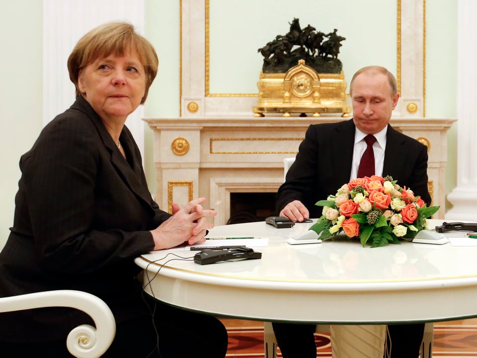 Am Runden Tisch: Bundeskanzlerin Angela Merkel blickt Ritchtung Kamera, Putin auf den Tisch. 