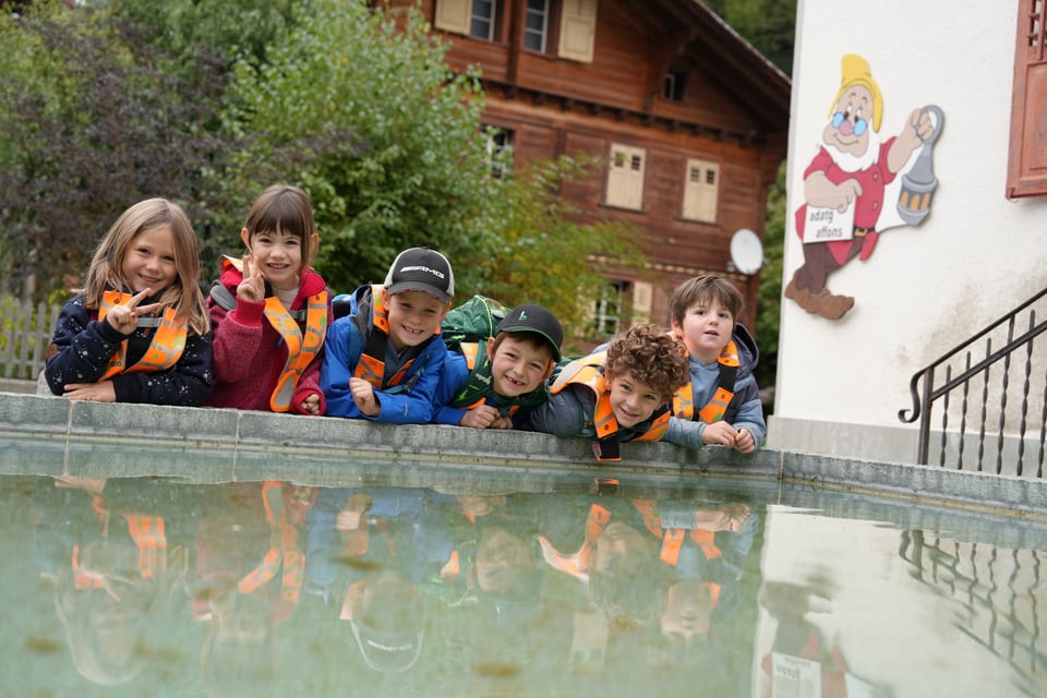 Eine Gruppe von Kindern posiert an einem Brunnen in einem alpinen Dorf.