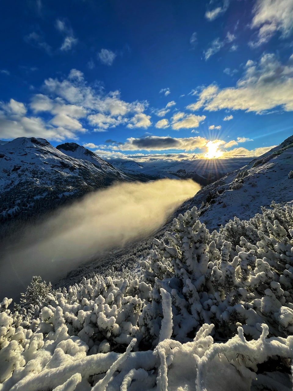 Gebirgslandschaft im Schnee mit Sonne und Nebel.