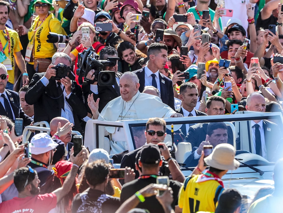 Der Papst fährt in einem Auto. Rundherum viele Menschen.
